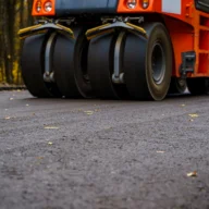 Máquina compactadora pavimentando uma via asfáltica em meio a árvores