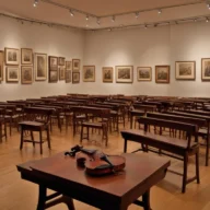 Espaço cultural com violas e objetos de museu em sala iluminada.