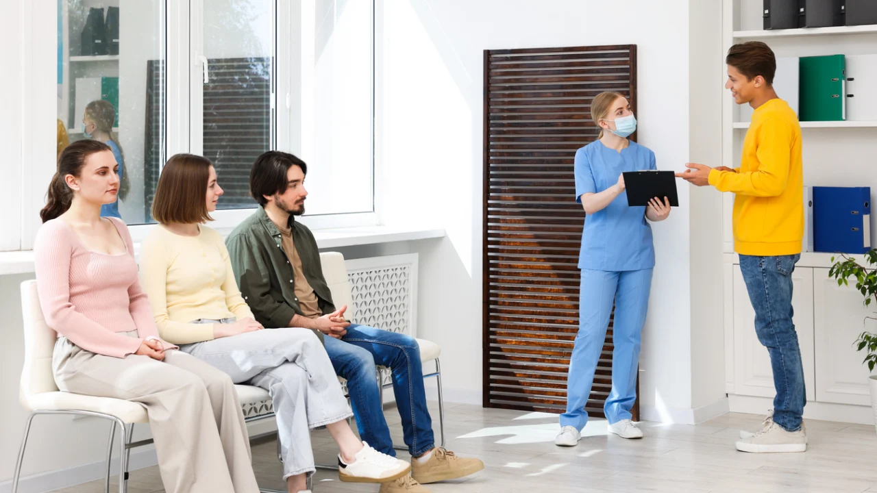 Sala de espera de unidade de saúde com mulheres aguardando atendimento e profissional de enfermagem com prancheta