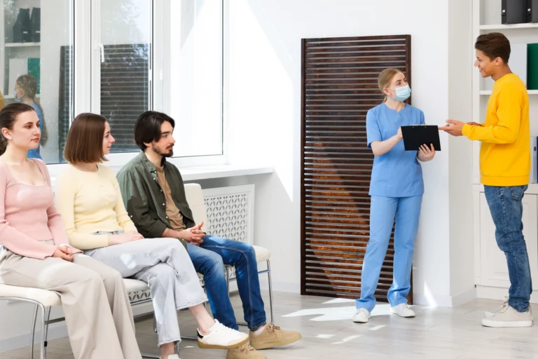 Sala de espera de unidade de saúde com mulheres aguardando atendimento e profissional de enfermagem com prancheta
