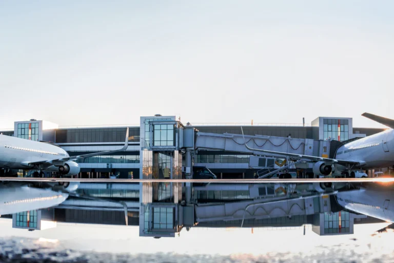 Aviões de passageiros estacionados em ponte de embarque de aeroporto, com reflexo no piso molhado ao amanhecer