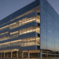 Fachada de vidro de edifício corporativo moderno ao anoitecer, com luzes acesas nos andares