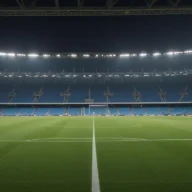Estádio de futebol vazio à noite, com o gramado iluminado pelos refletores e arquibancadas ao fundo