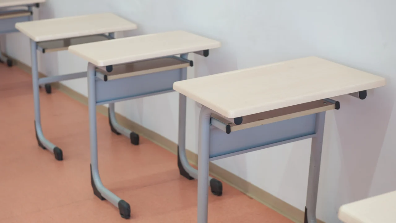 Carteiras enfileiradas em sala de aula vazia de escola pública, com luz natural pela janela
