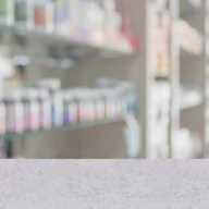 Balcão de farmácia de unidade pública de saúde à noite, com prateleiras de medicamentos ao fundo desfocadas