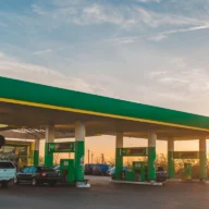 Posto de gasolina de bairro em Atibaia ao amanhecer, com bombas de combustível alinhadas e pista molhada pela chuva fina