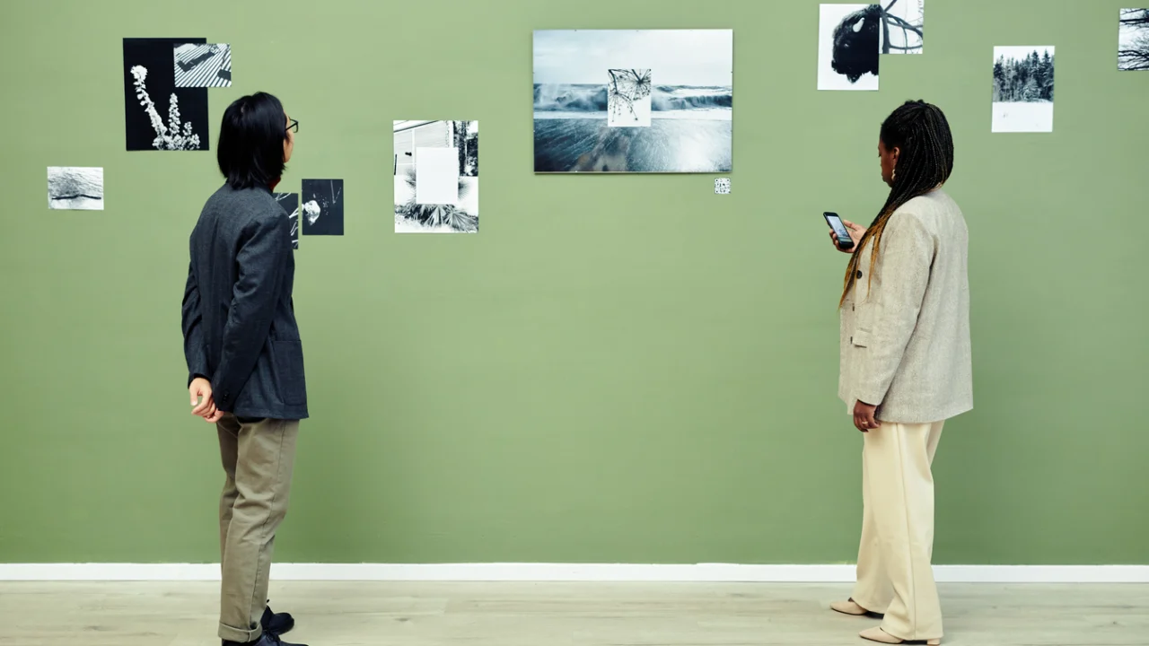 Visitantes observam painéis com fotografias em preto e branco expostos em parede verde