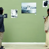 Visitantes observam painéis com fotografias em preto e branco expostos em parede verde