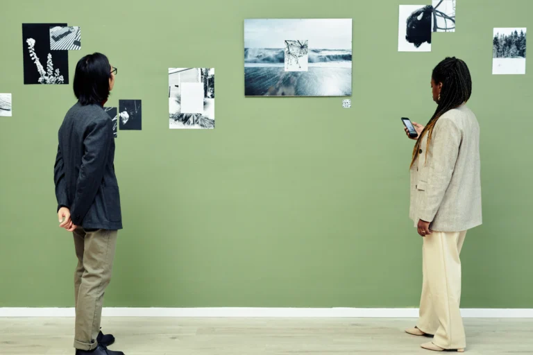 Visitantes observam painéis com fotografias em preto e branco expostos em parede verde