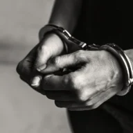 Mãos algemadas de homem detido, em registro fotográfico em preto e branco