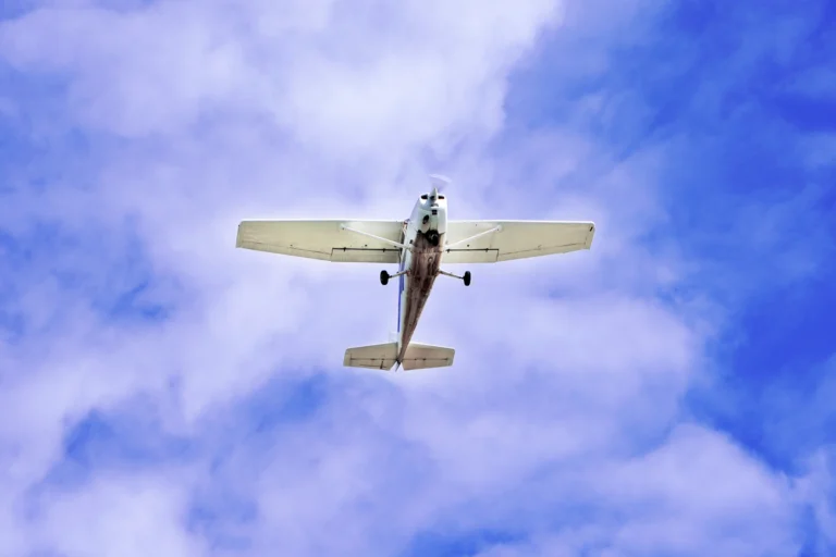 Avião monomotor branco em pleno voo contra um céu azul com nuvens