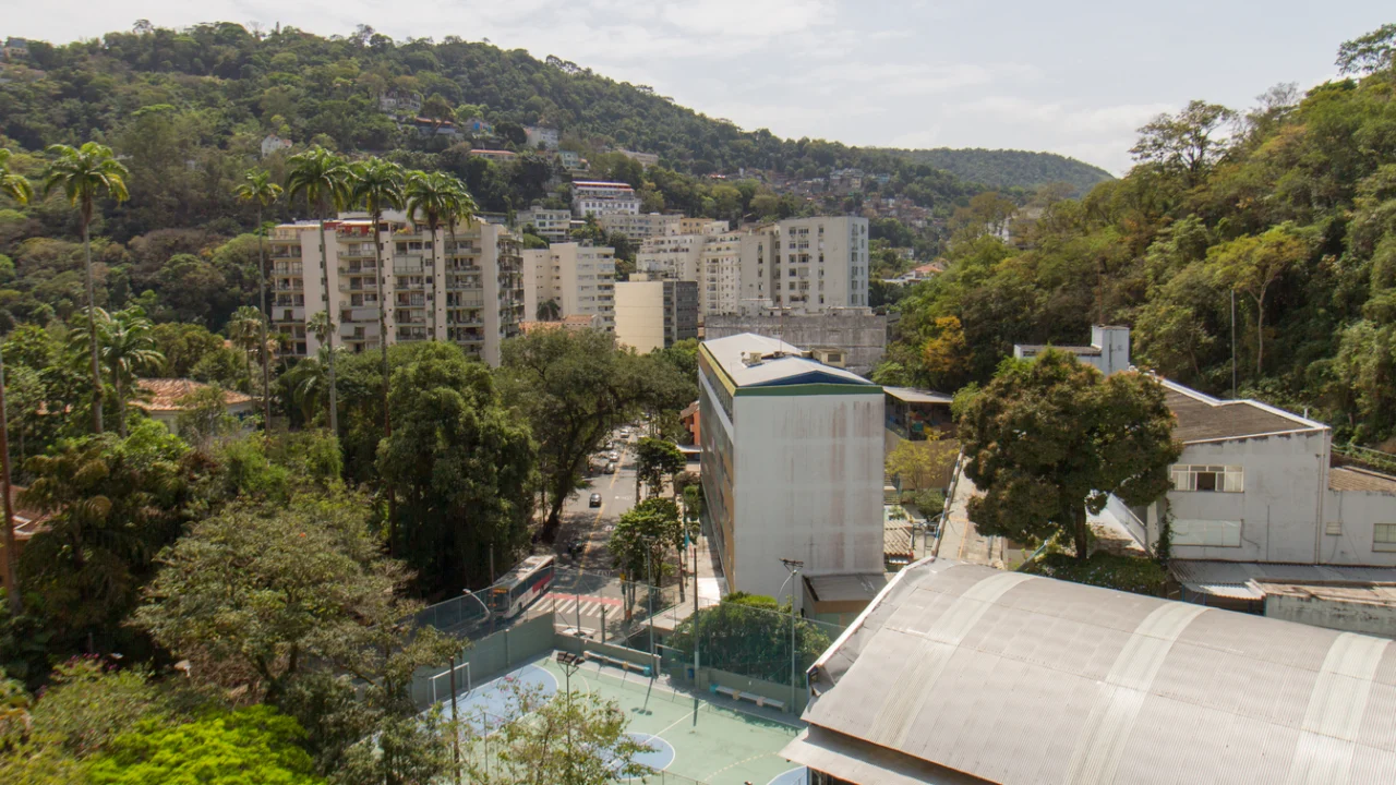 Vista aérea de bairro residencial brasileiro com prédios, árvores e rua movimentada ao pé de um morro
