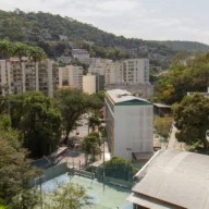 Vista aérea de bairro residencial brasileiro com prédios, árvores e rua movimentada ao pé de um morro