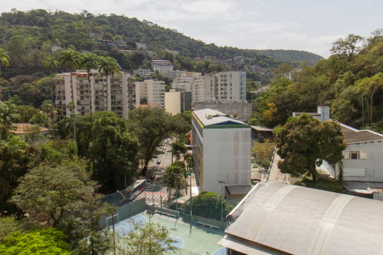 Vista aérea de bairro residencial brasileiro com prédios, árvores e rua movimentada ao pé de um morro