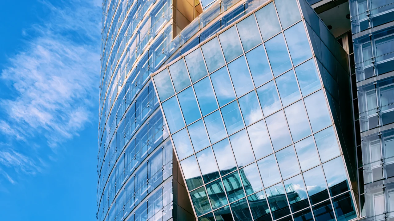 Fachada de torre corporativa de vidro azul refletindo o céu, vista de baixo