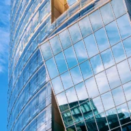 Fachada de torre corporativa de vidro azul refletindo o céu, vista de baixo