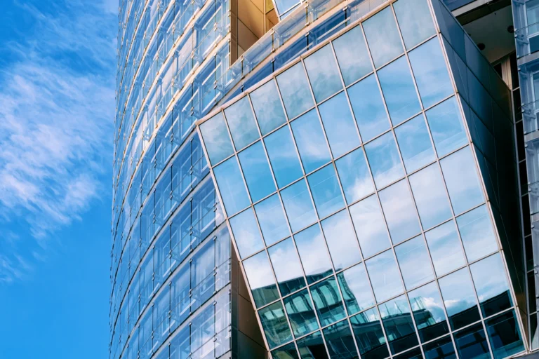 Fachada de torre corporativa de vidro azul refletindo o céu, vista de baixo