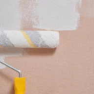 Parede de alvenaria sendo pintada com rolo e tinta branca durante serviço de manutenção