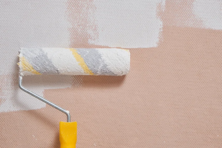Parede de alvenaria sendo pintada com rolo e tinta branca durante serviço de manutenção