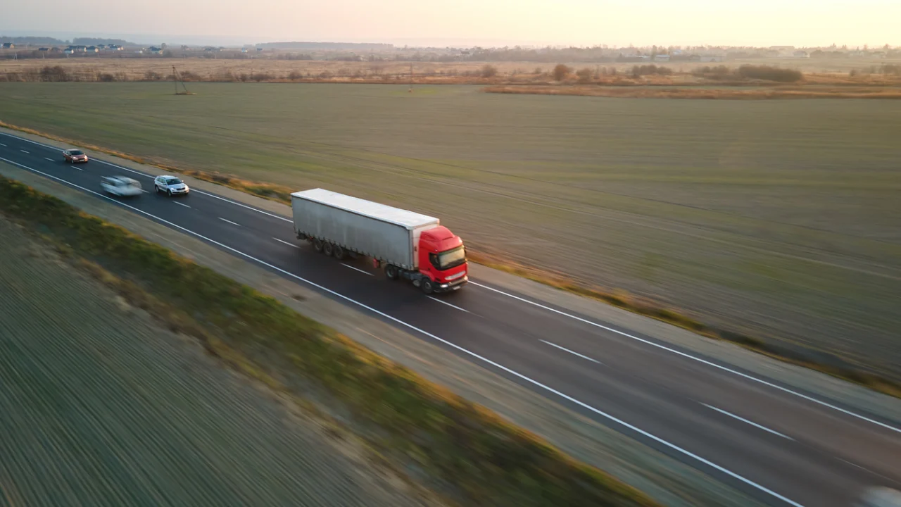 Caminhão de carga trafega em rodovia de pista dupla cercada por plantações ao entardecer