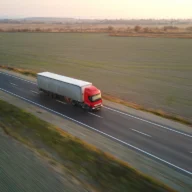 Caminhão de carga trafega em rodovia de pista dupla cercada por plantações ao entardecer