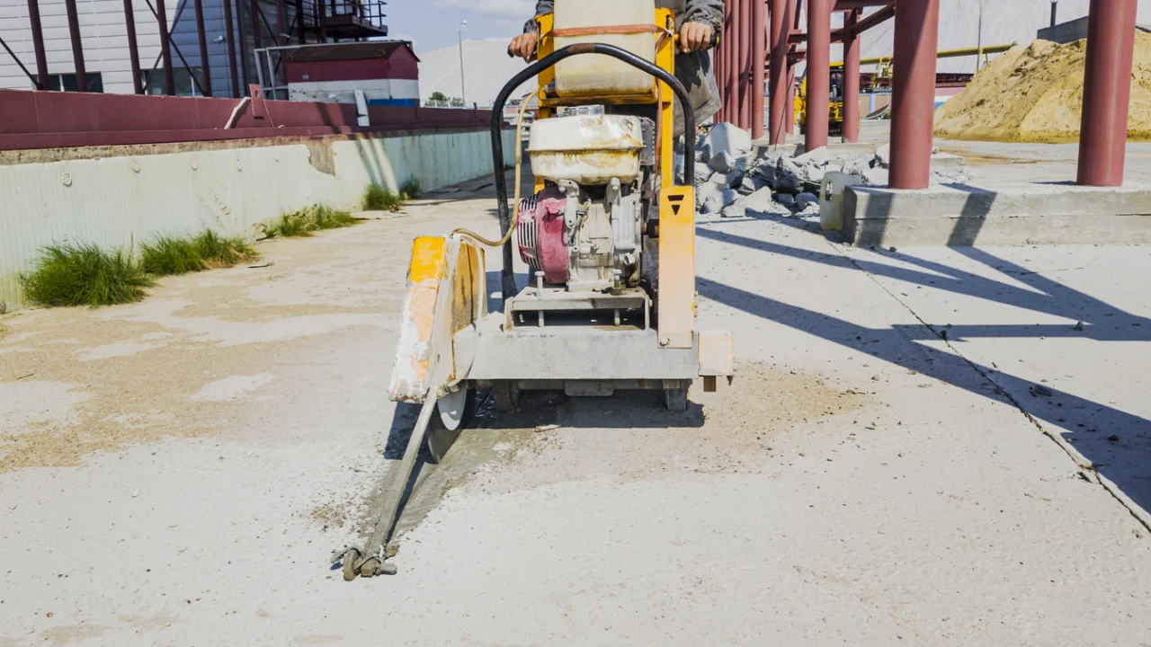 Máquina de corte de concreto em obra de pavimentação, com trabalhador ao fundo
