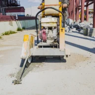 Máquina de corte de concreto em obra de pavimentação, com trabalhador ao fundo