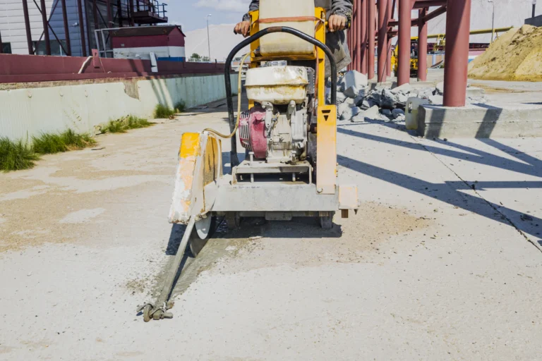 Máquina de corte de concreto em obra de pavimentação, com trabalhador ao fundo