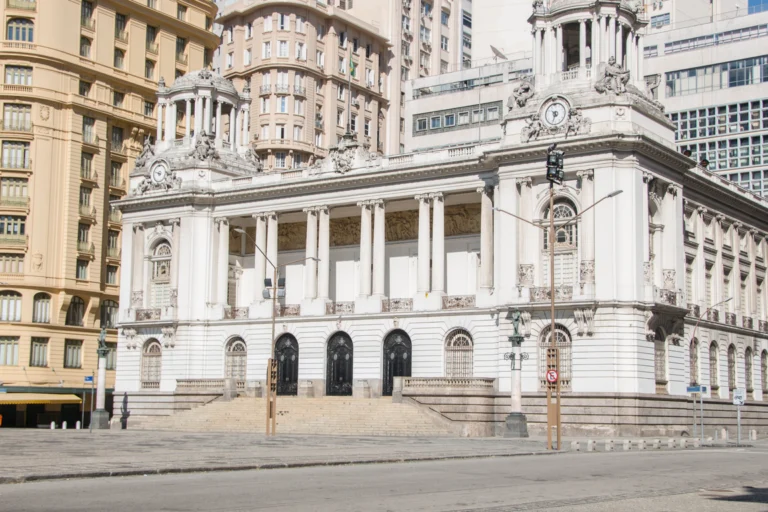 Fachada de prédio público com colunas e escadaria, vista da calçada em dia de sol