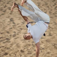 Atleta de capoeira executa movimento acrobático em área de areia