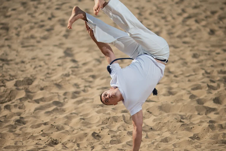 Atleta de capoeira executa movimento acrobático em área de areia