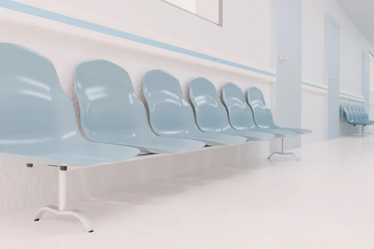 Sala de espera de um posto de saúde, com cadeiras de plástico azuis enfileiradas ao longo de um corredor claro