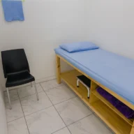 Sala de atendimento com maca coberta por lençol azul, cadeira e armário de madeira