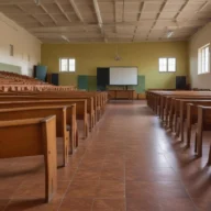 Sala ampla com fileiras de carteiras escolares de madeira vazias e tela branca ao fundo