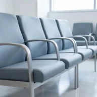 Cadeiras azuis enfileiradas em sala de espera de hospital com luz natural