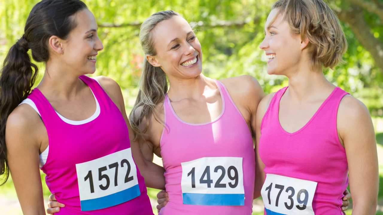 Grupo de mulheres sorrindo durante corrida de rua em camisetas rosas