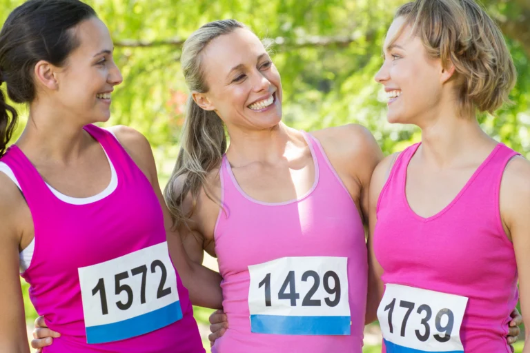 Grupo de mulheres sorrindo durante corrida de rua em camisetas rosas