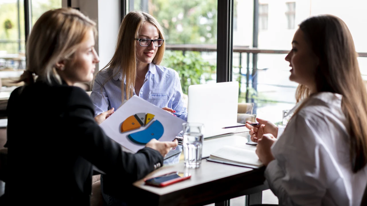 Mulheres conversando em reunião de negócios à mesa, em salão iluminado