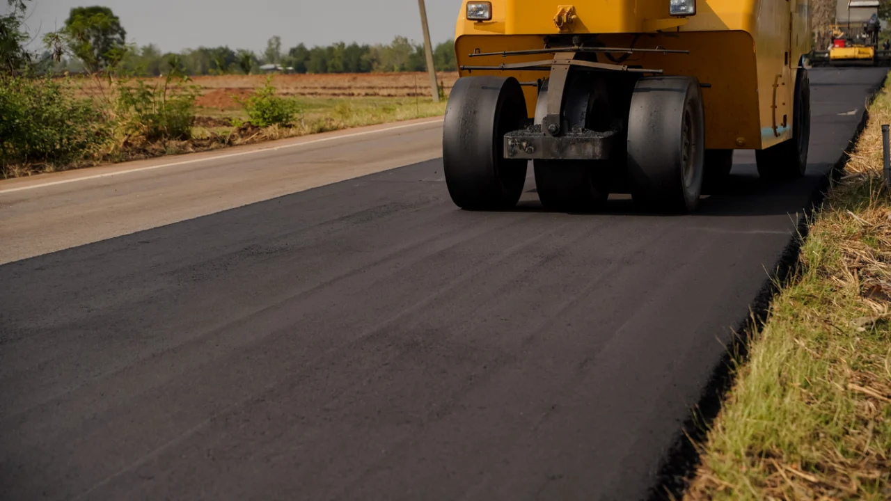 Máquina e rolo compactador em obra de recapeamento de estrada rural