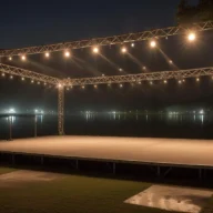 Palco iluminado montado à beira de um lago à noite, com estrutura de metal e refletores acesos