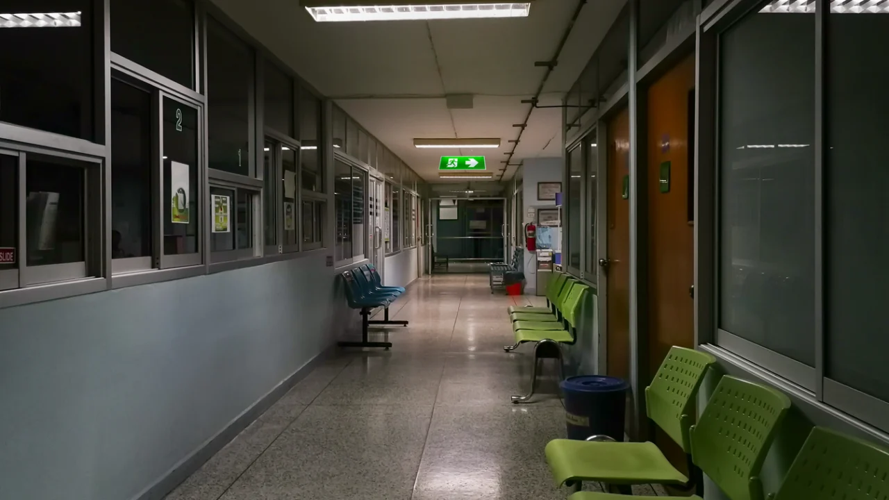 Corredor vazio de hospital à noite com cadeiras de espera e sinal de saída iluminado