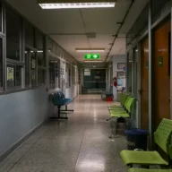 Corredor vazio de hospital à noite com cadeiras de espera e sinal de saída iluminado