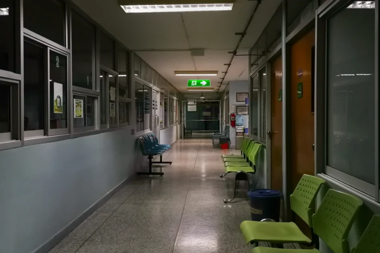 Corredor vazio de hospital à noite com cadeiras de espera e sinal de saída iluminado