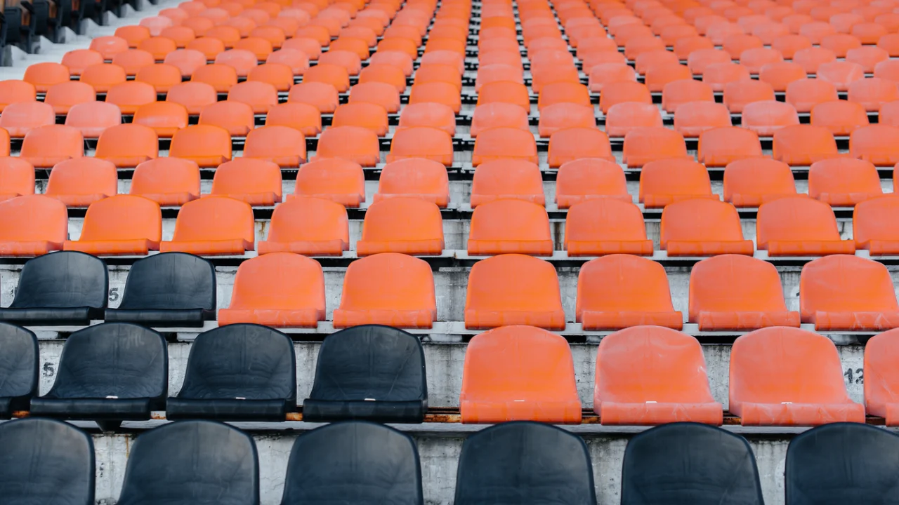 Arquibancadas de estádio de futebol com cadeiras laranjas e pretas vazias
