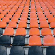 Arquibancadas de estádio de futebol com cadeiras laranjas e pretas vazias