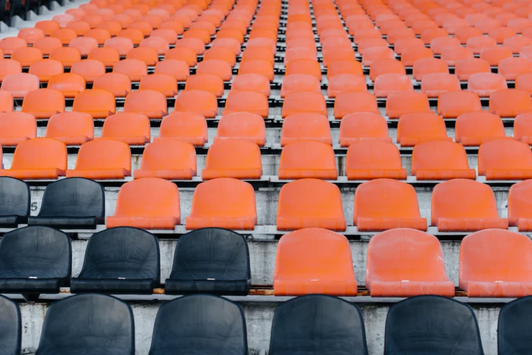 Arquibancadas de estádio de futebol com cadeiras laranjas e pretas vazias