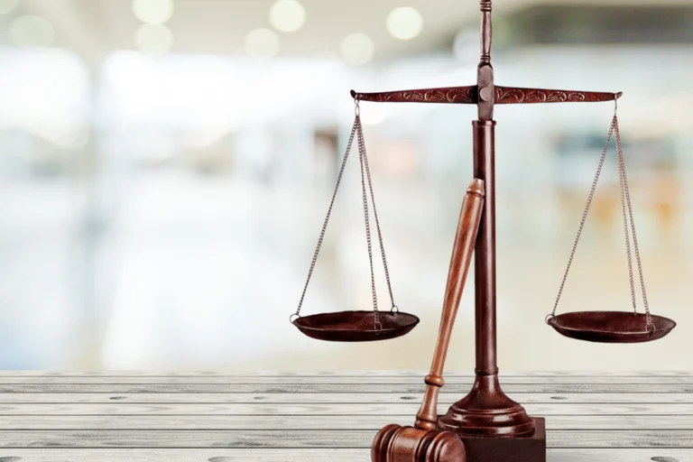Balança da justiça e martelo de juiz sobre mesa de madeira clara