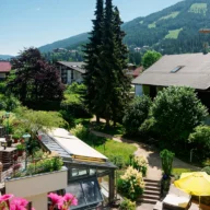 jardim e fachada de uma pousada em cidade serrana, com flores, guarda-sóis e montanhas ao fundo