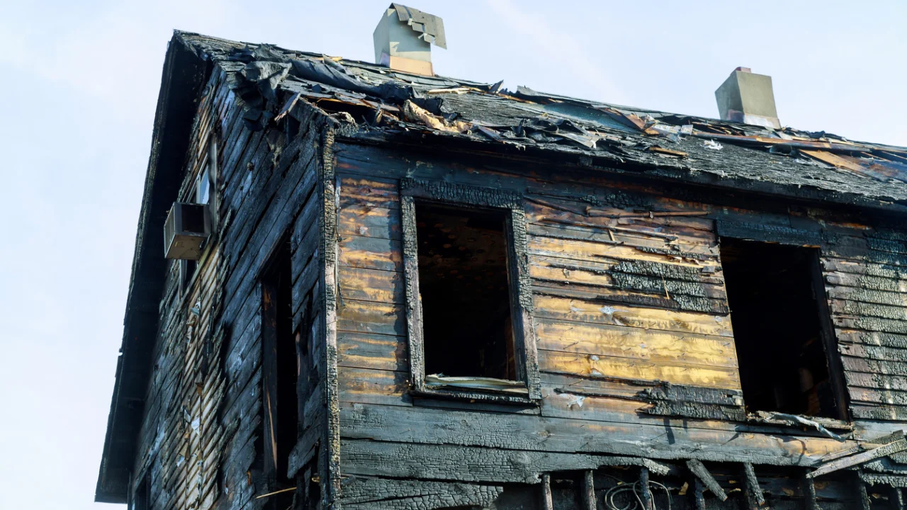 Estrutura de madeira de uma casa destruída pelo fogo, vista da rua ao amanhecer