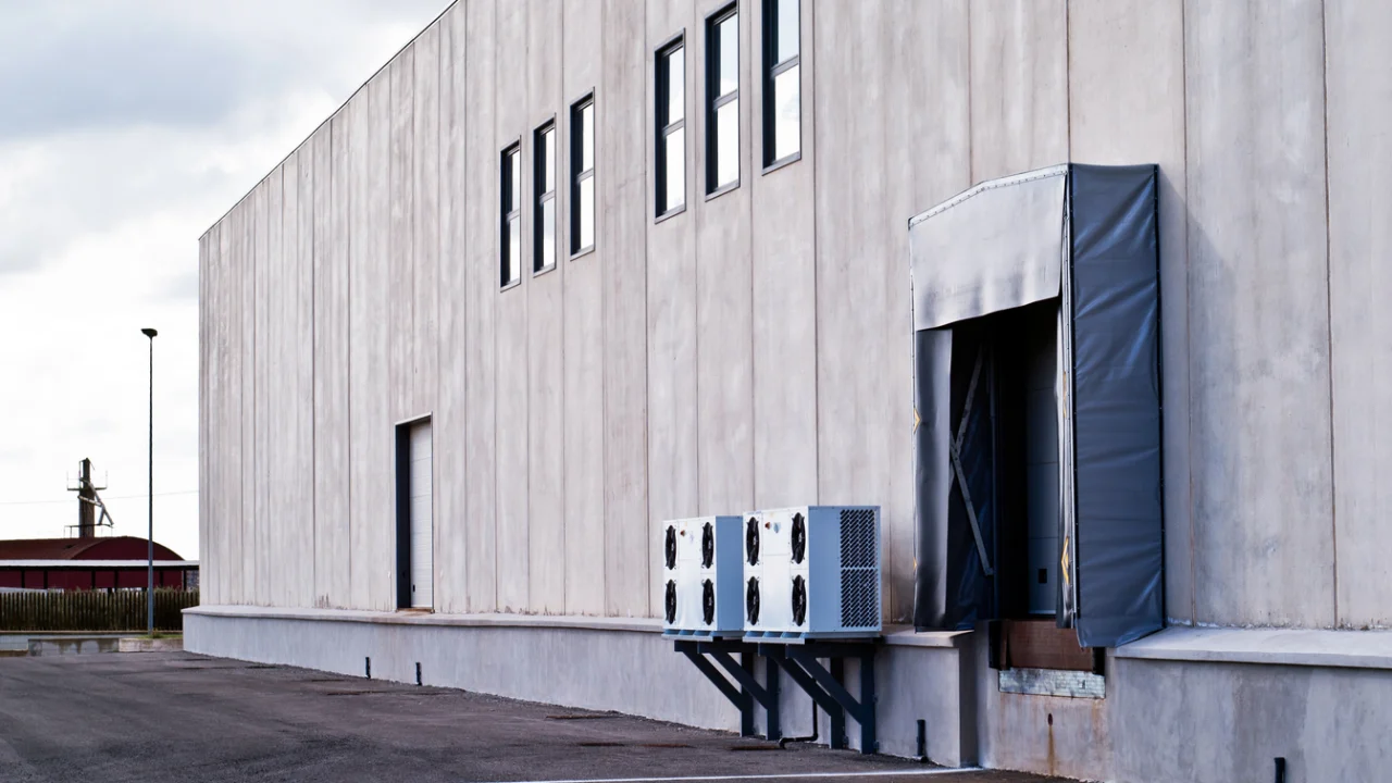 Fachada de galpão industrial de concreto com doca de carga e ar-condicionado externo, em dia nublado